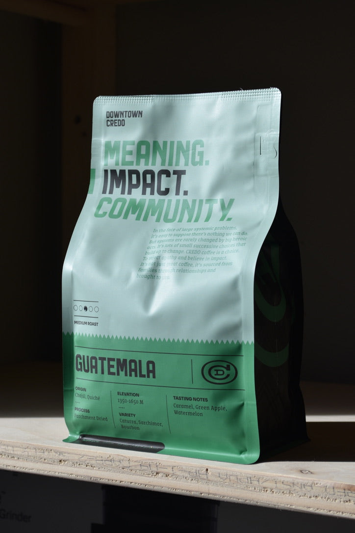 A packaged bag of Guatemala coffee beans with a label that includes the words 'Meaning. Impact. Community.'