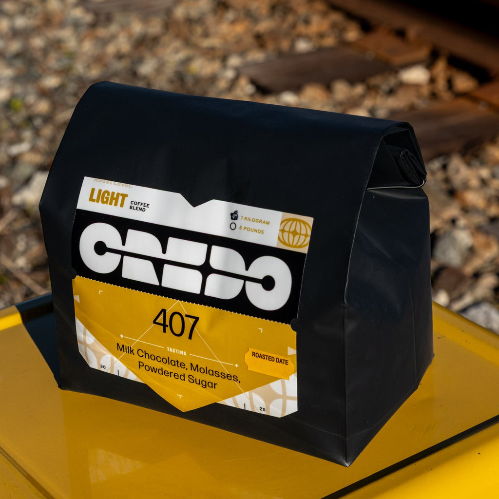 Black bag of CREDO 407 coffee on a yellow surface with train tracks in the background