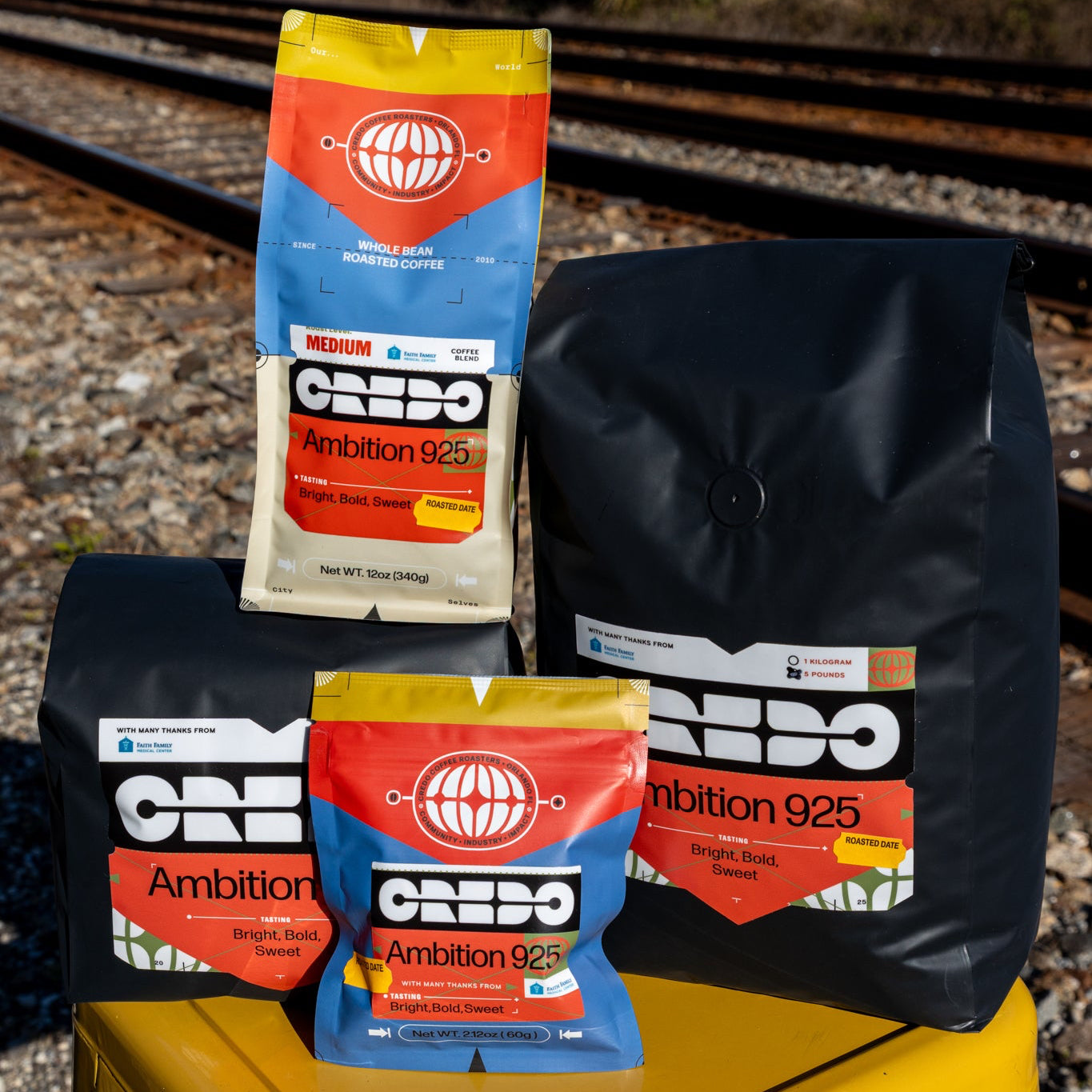 CREDO Ambition 925 coffee packages on a yellow stool with train tracks in the background