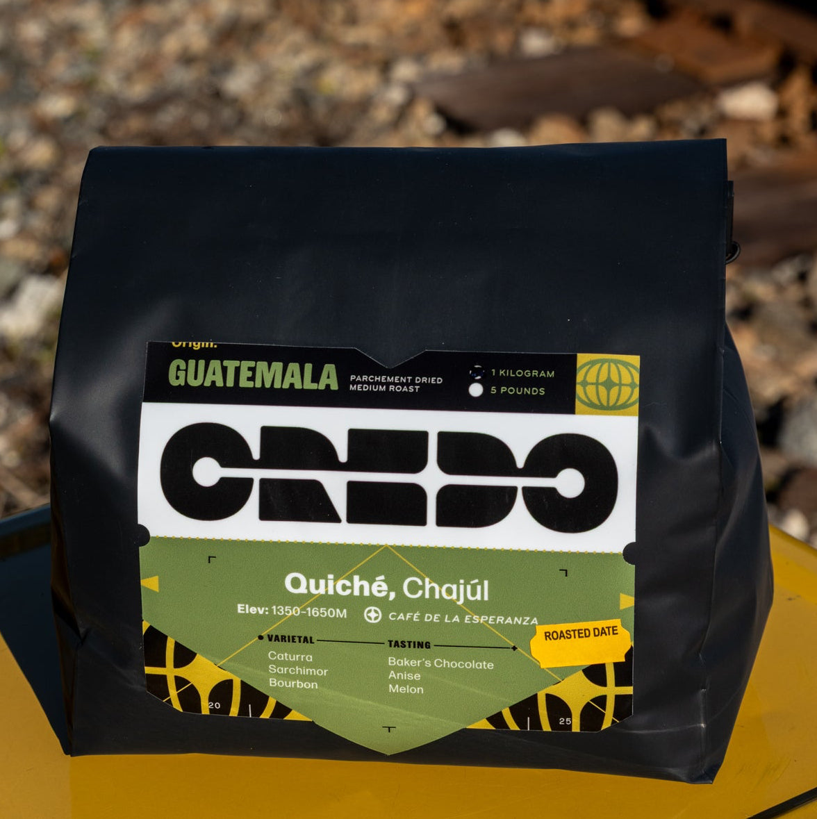 Coffee package with 'Guatemala' and 'CREDO' branding on a yellow surface with train tracks in the background.
