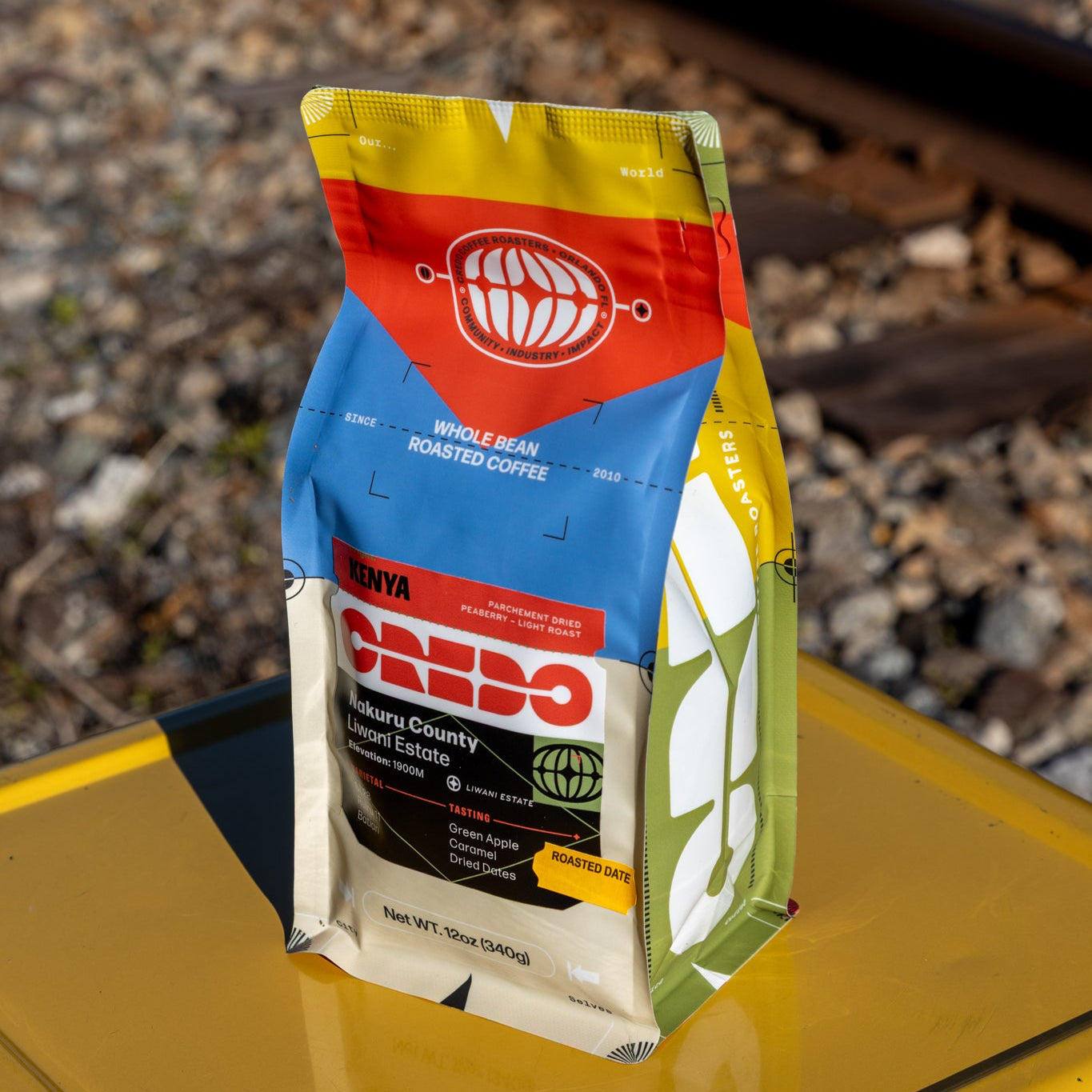 Caffeo coffee package on a yellow surface with railway tracks in the background
