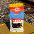 Coffee bag with visible branding on a yellow surface with railway tracks in the background