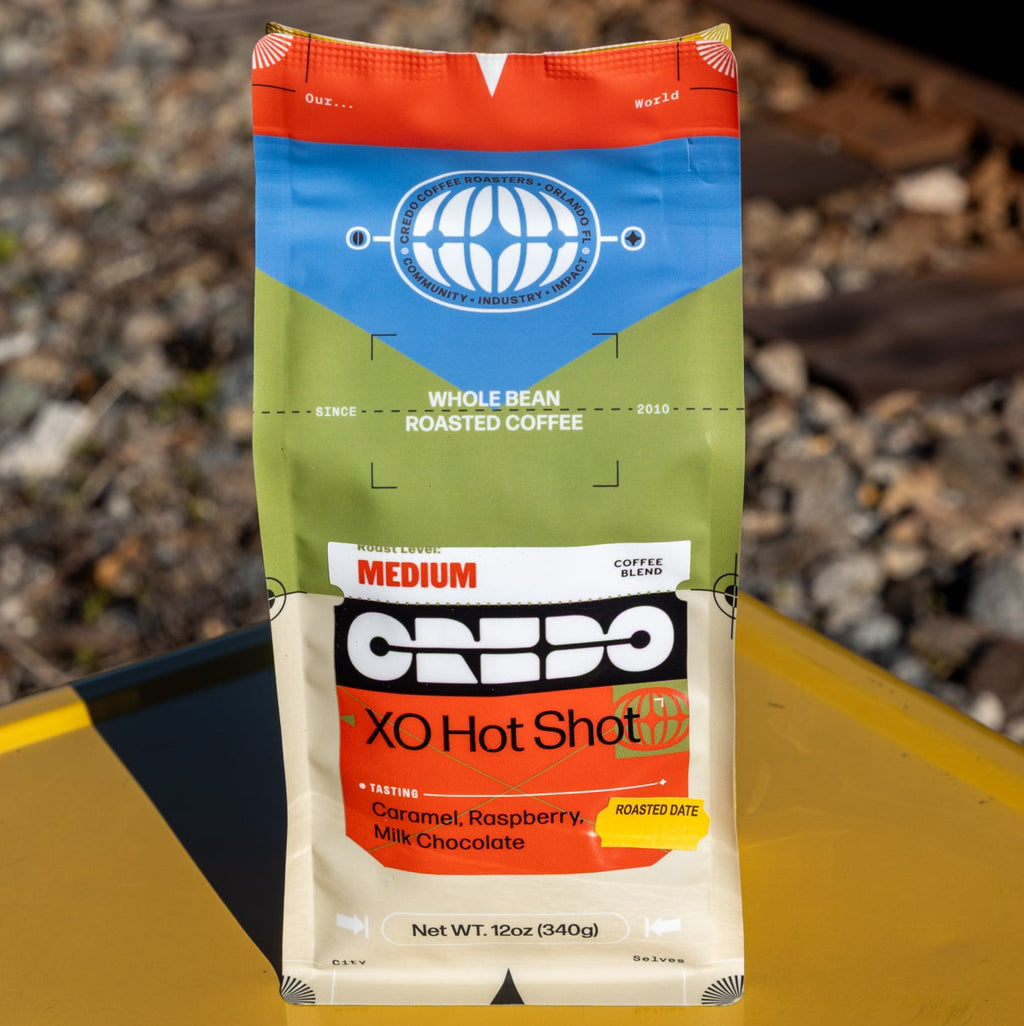CREDO XO Hot Shot coffee package on a yellow surface with train tracks in the background