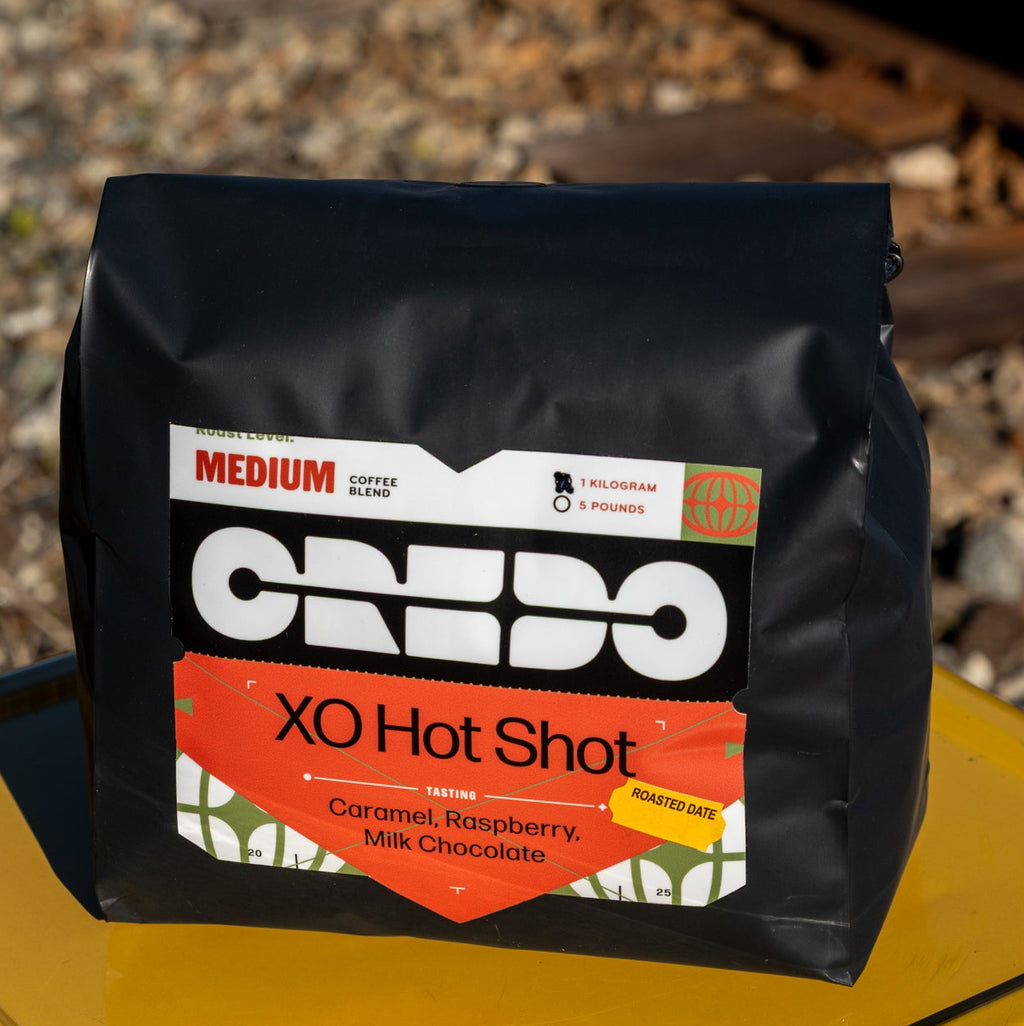 CREDO XO Hot Shot coffee package on a yellow surface with train tracks in the background