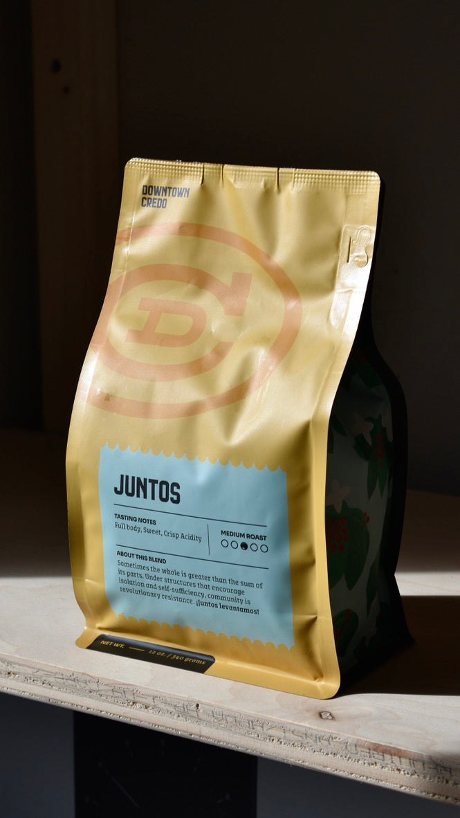 A sealed, gold-colored bag of coffee labeled 'JUNTOS' by Credo Coffee Roasters.